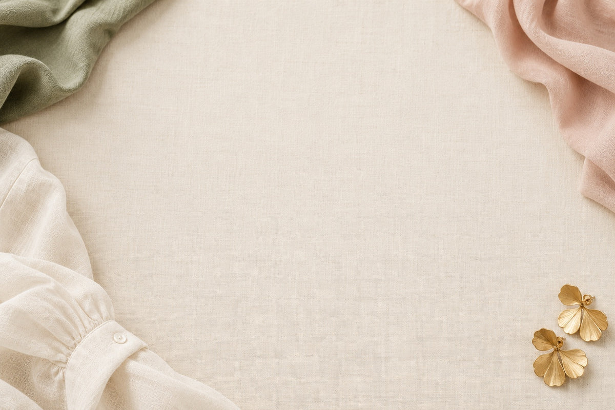 Soft ivory linen, blush and sage fabrics with gold earrings framing a clear centre